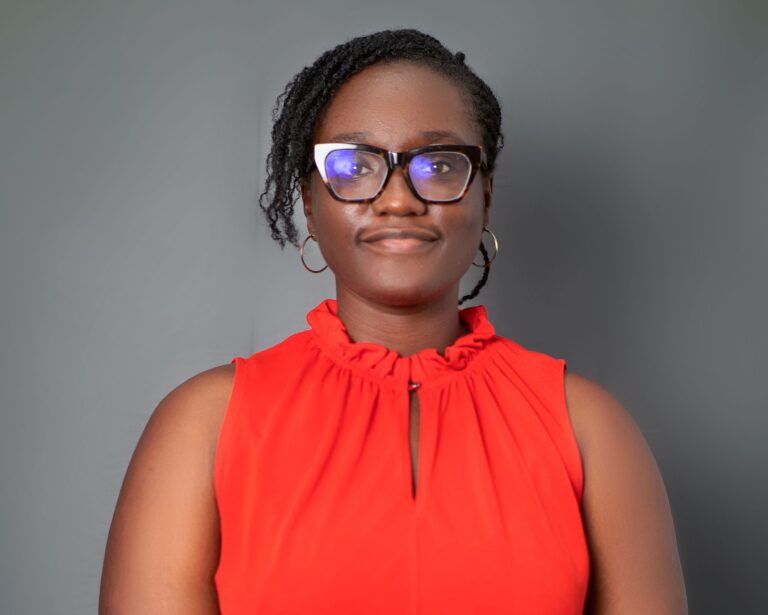 A woman in red shirt wearing glasses and smiling.