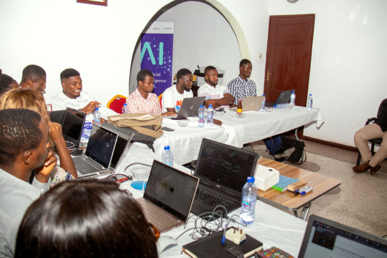 A group of people sitting around tables with laptops.